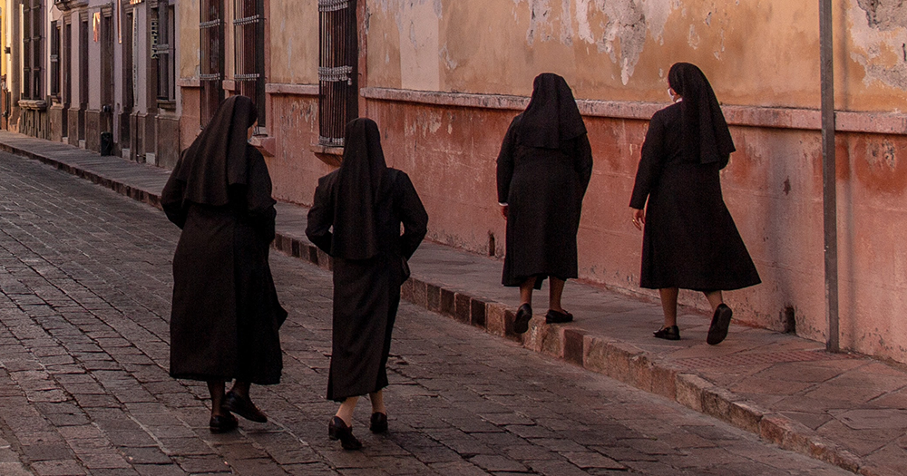 The image shows four nuns walking on a road.