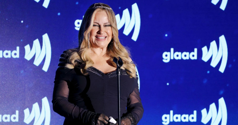 Jennifer Coolidge at the GLAAD Media Awards ceremony, standing in front of a blue background in a black dress.