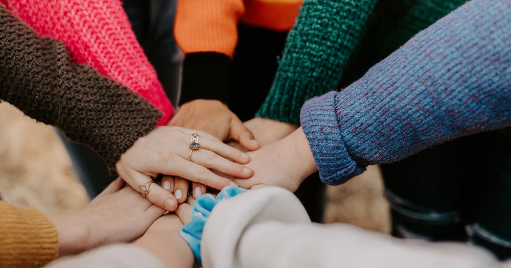This article is about youth workers supporting LGBTQ+ people in Ireland. In the photo, the hands of young people gathered on top of each other.