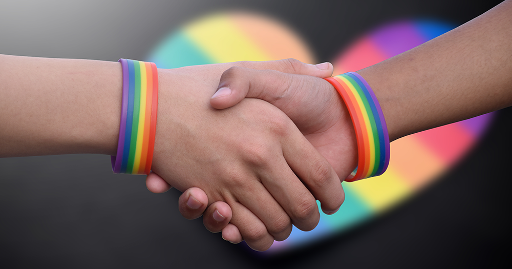 Close up of handshake with rainbow LGBTQIA+ wristbands on arms.