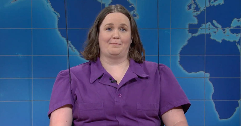 A screenshot of Molly Kearney, the first non-binary cast member of SNL. They have a brown bob and are wearing a purple shirt.