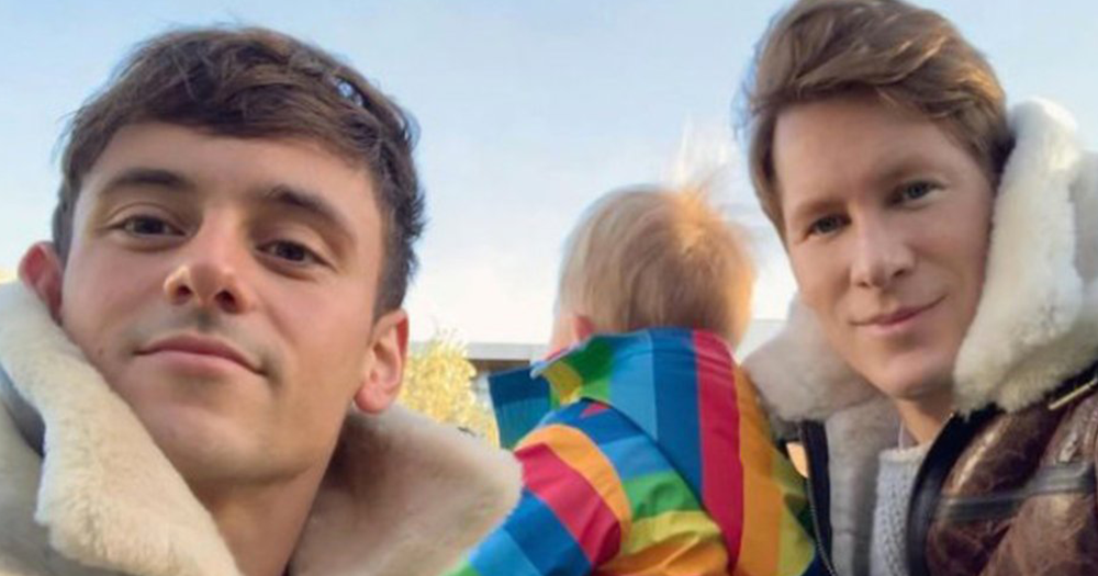 Tom Daley and Dustin Lance Black smile toward camera and hold baby in rainbow outfit, they announced that they have welcomed their second child.