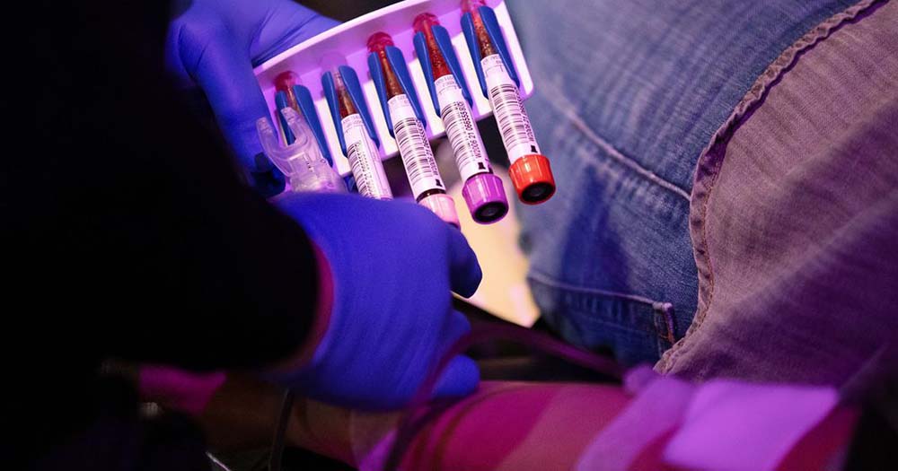 Two gloved hands hold a tray of blood vials representing the US updated policy which allows donations from some gay and bisexual men.