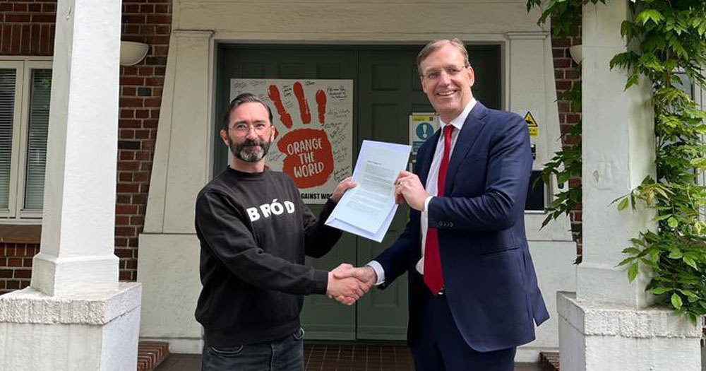 The image shows Jed Dowling, Festival Director of Dublin Pride, receiving a diplomatic statement from the ambassador of the Netherlands. The pair are standing in a doorway shaking hands and holding the letter between them.