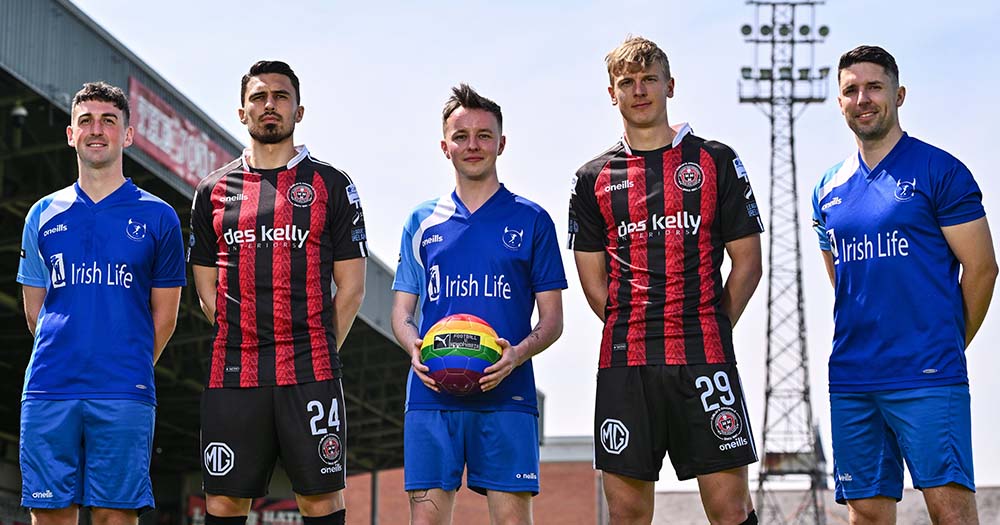 Football players in blue and red jerseys stand side by side with rainbow coloured football ahead of Dublin Pride season.
