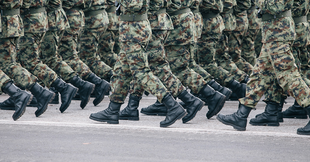 This story is about France lifting the ban on HIV Positive people joining the military. The image shows an army of camouflage trousers walking together.