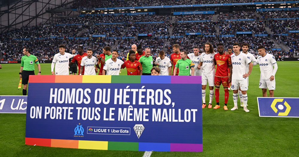 French soccer clubs posing for a campaign against homophobia, with a banner in the colours of the rainbow that reads a message of support in French.