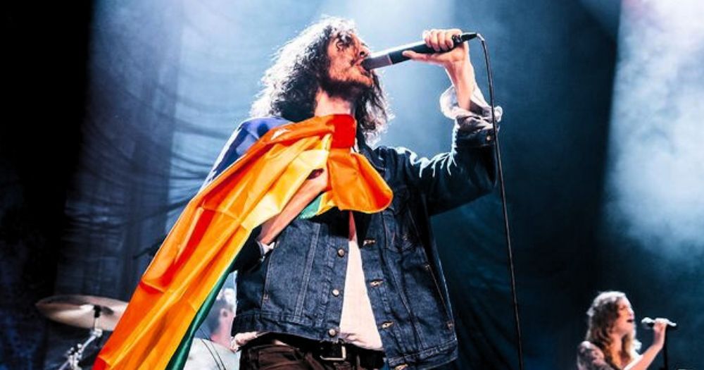 Photo of Hozier holding a LGBTQ+ flag while performing on stage