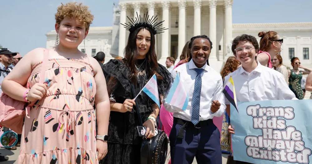 Four students wearing gender-affirming clothing stand in front of capitol building for their trans youth prom.