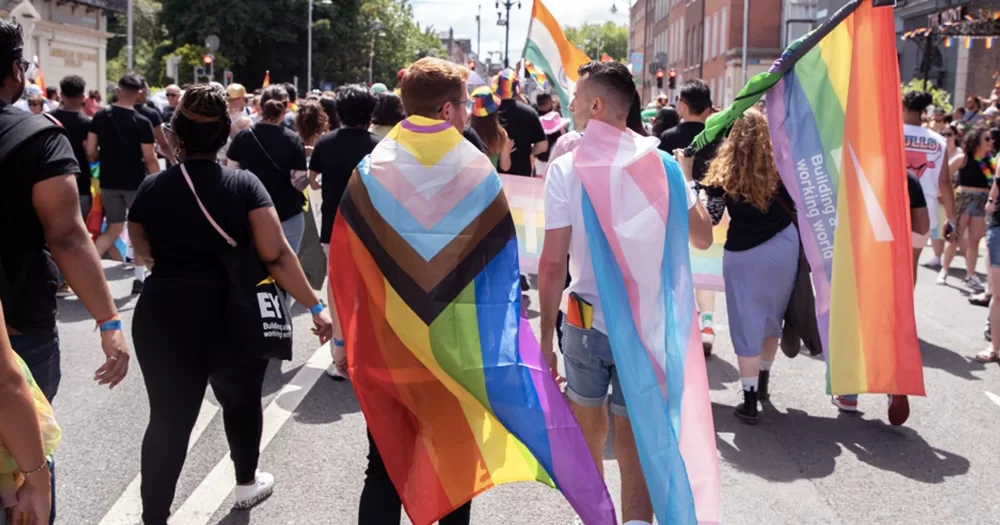 People marching at the Dublin Pride parade 2023, with two people wearing a progress Pride flag and a trans flag.