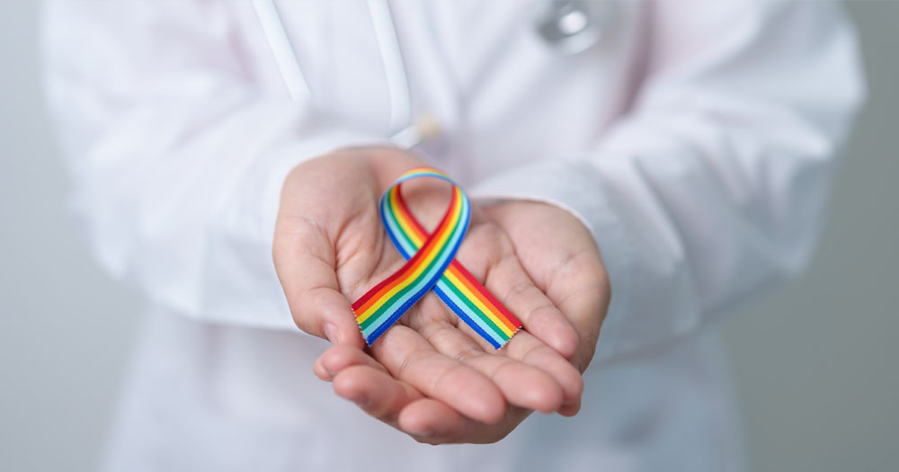 Man2Man has launched a pre-Pride campaign to raise awareness of Shigella. The photo shows a person in a white coat with a stethoscope and holding a Pride ribbon in their hands.