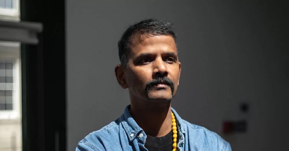 Pradeep Mahadeshwar, founder of Queer Asain Pride Ireland. H eis wearing an open denim shirt with a black t-shirt and a yellow bead necklace.