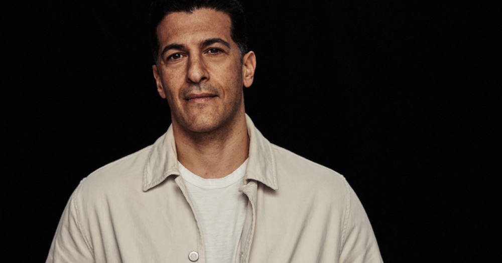 Actor Simon Kass, looking at the camera wearing a shirt, on a black background.