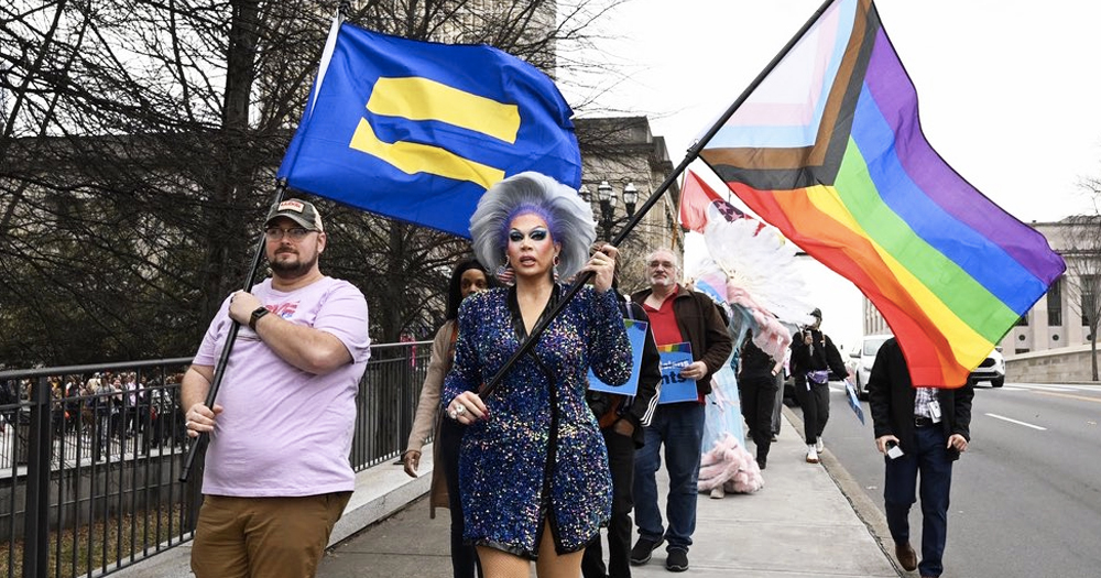 People protesting against an anti-drag law in Tennessee that was deemed unconstitutional, walking down a street waving a progress Pride flag.
