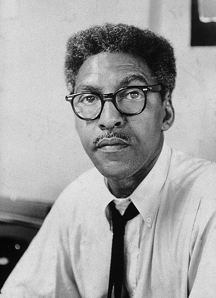 LGBTQ+ historical figures, Bayard Rustin looks at the camera wears glasses and a suit and tie.