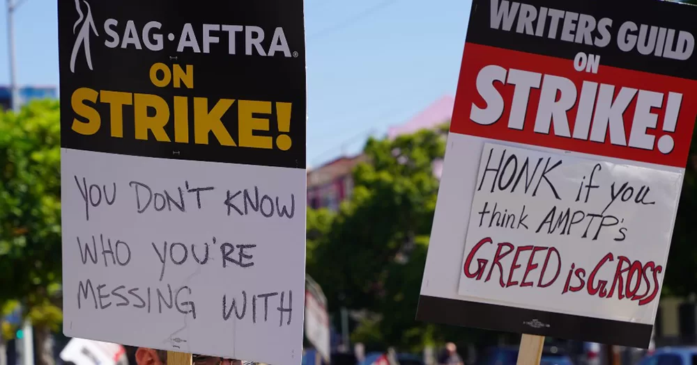 Two signs from the picket lines of the 2023 SAG-AFTRA and WGA strike, one reading 
