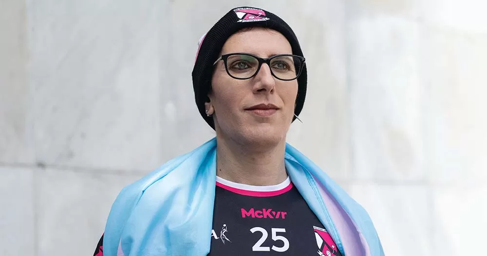 Giulia Valentino poses wearing GAA jersey and trans flag across shoulders