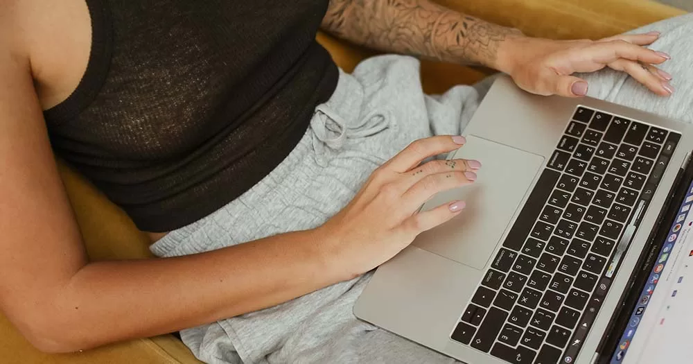 Person with tattoos wearing black tank top holding laptop representing EU LGBTQ survey