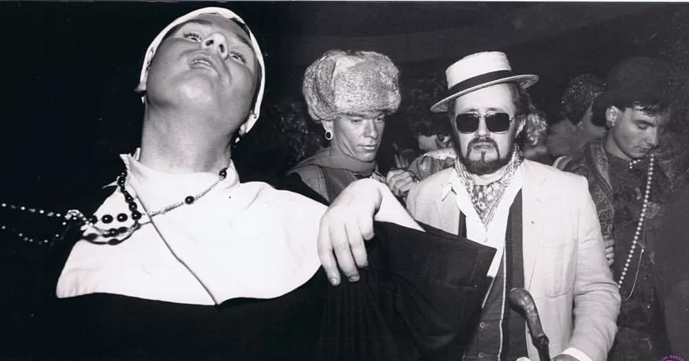 A photo taken at one of the sites on Tonie Walsh's new queer history walking tour of Dublin. The black and white image shows partygoers in fancy dress at the 1988 Halloween Ball. One man is dressed as a nun, one is wearing a Russian style fur hat and one is wearing a straw boating hat and sunglasses.