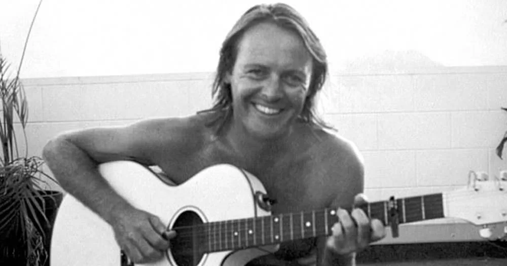 Black and white photo of AC/DC band manager Crispin Dye playing the guitar, he was killed in a potential hate crime in 1993.