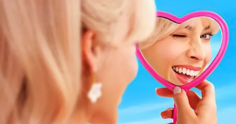 A promotional photo for Barbie, Ireland's most successful box office film ever. The image shows Margot Robbie as Barbie holding a pink heart-shaped hand mirror, in which we see the reflection of her winking and smiling.