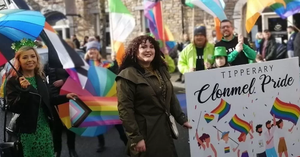 Clonmel, Derry and Yougal Pride all take place this Saturday. This image shows a group maarching from Clonmel Pride at a St Patrick's Day event. The group are carrying rainbow flags and umbrellas, with a banner saying Clonmel Pride.