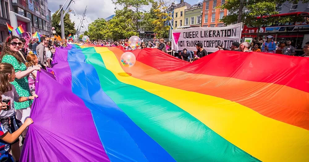 People hold edges of rainbow flag that stretches across road ahead of Cork Pride 2023.