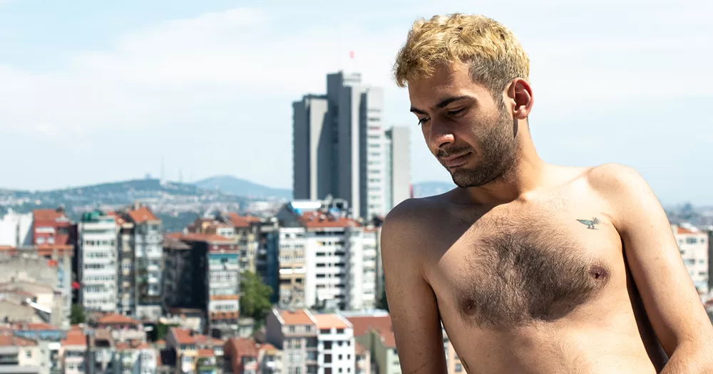 An Elska Instanbul participant poses shirtless in front of the city skyline.