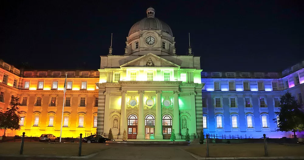 Irish government buildings lit up in Pride rainbow colours on a dark night.