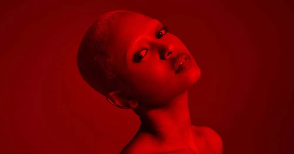 A head shot of singer and songwriter Kelela, a woman with a shaved head, in red lighting.