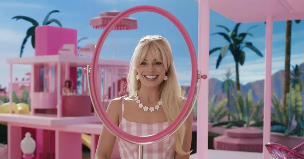 Margot Robbie as Barbie in the Barbie movie that is to be banned in Lebanon, in front of a mirror, wearing a pink dress and a white necklace.