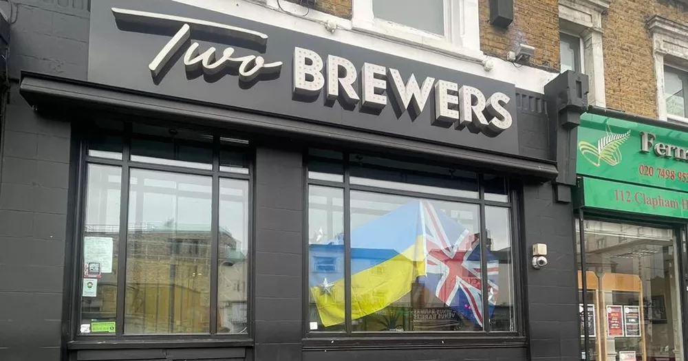 The exterior of Two Brewers in South London where two men were stabbed. The building is black with the name of the venue written in silver. There is a Ukrainian flag and Union Jack flag in the window.