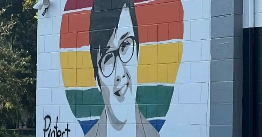A defaced mural of Lyra McKee, with a black and white image of the journalist painted over a rainbow heart.