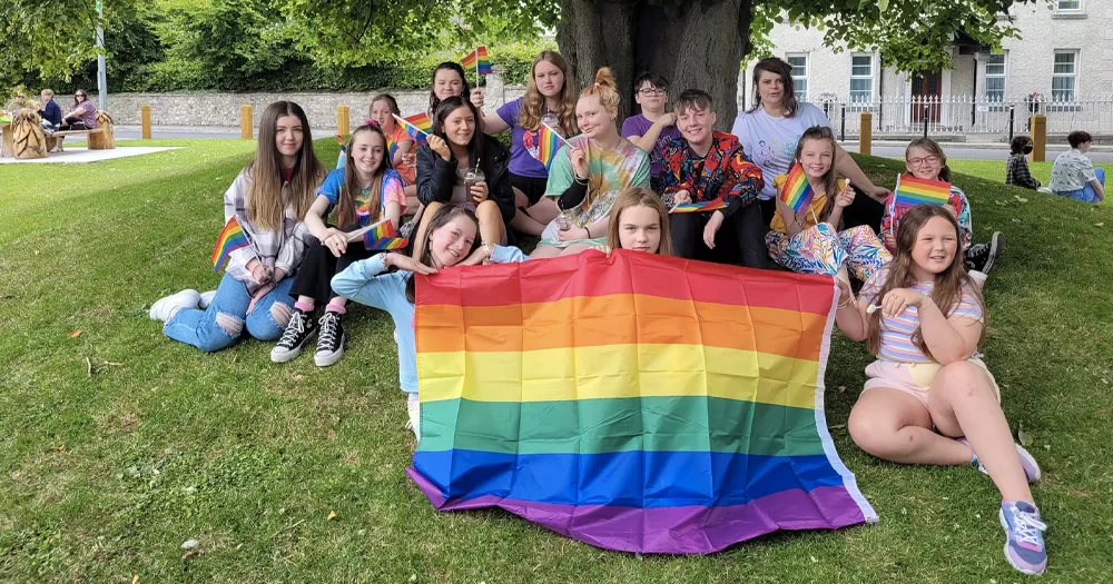 Photo taken at Meath Pride, which this year was disrupted by anti-LGBTQ+ protesters, with teenagers holding a rainbow flag while sitting on the grass.