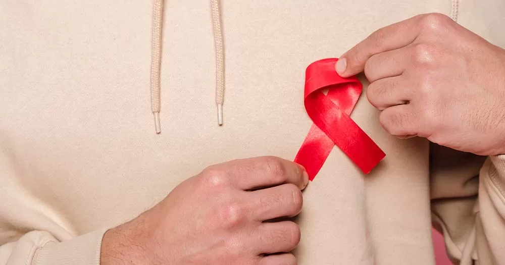 Two hands positioning red ribbon on shirt, Gay Health conference announced their 2023 speakers