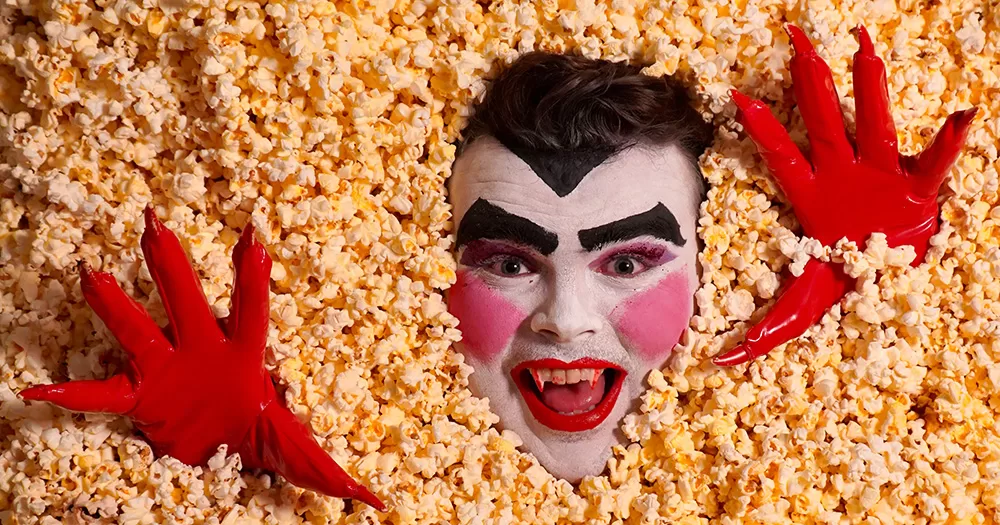 A promotional image from Scaredy Fat. It shows a person's face and hands emerging from a big pile of popcorn.