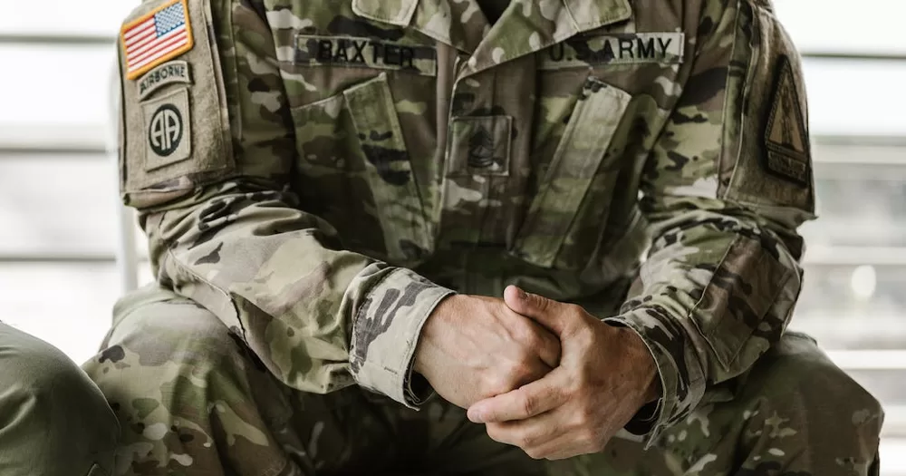This article is about LGBTQ+ veterans suing the Pentagon. In the photo, a US soldier sitting in uniform with their hands clasped.
