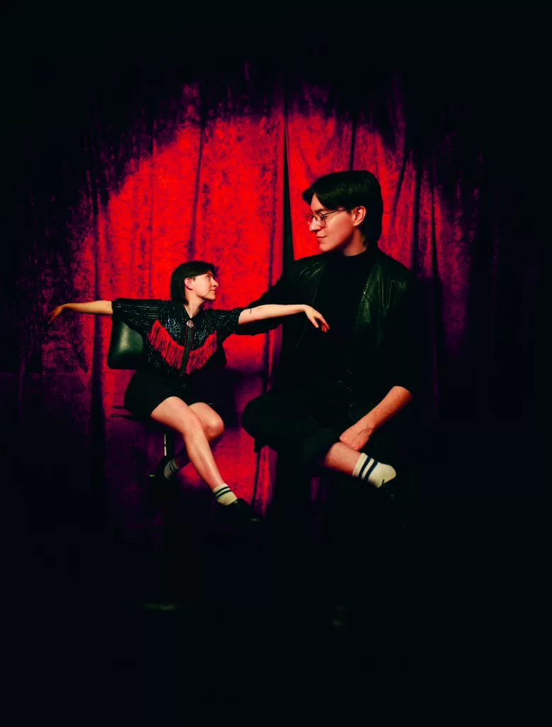 Dublin Fringe 2023 performer Aoife O'Connor poses in front of a red curtain, holding a puppet of themself.