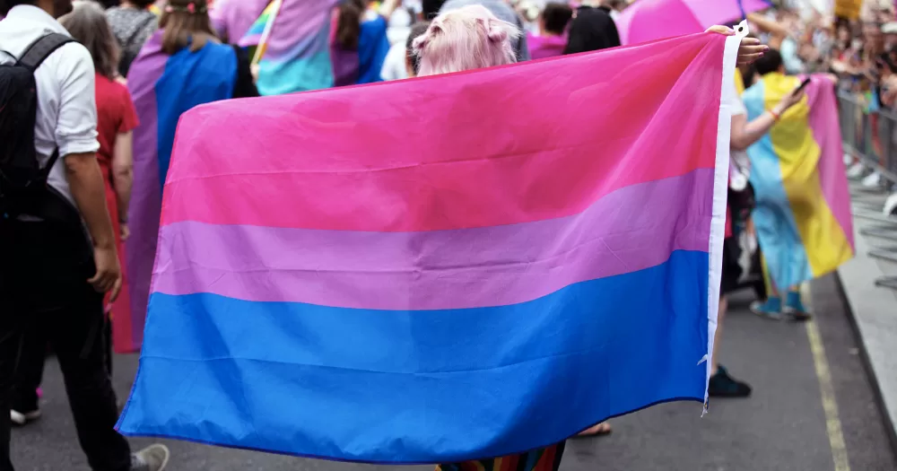 This article is about the impact of biphobia on bisexual people. In the photo, a person holding a Bi flag at a parade.