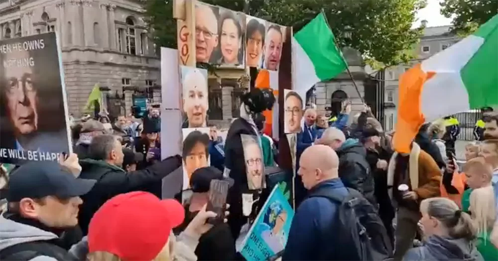 Mock gallows being brought to the Dáil. The image shows a crowd of people gathered around the wooden structure, and Irish flags can be seen on poles.
