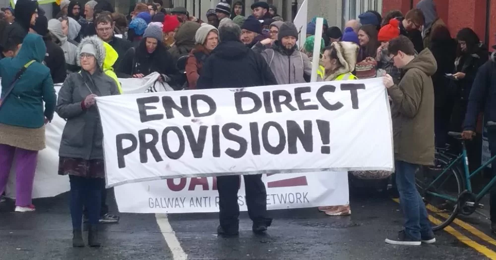 A group of protestors hold an 'END DIRECT PROVISION' banner.