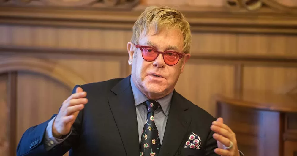 Photograph of Elton John wearing suit and pink glasses, he issued a statement in response to Suella Braverman