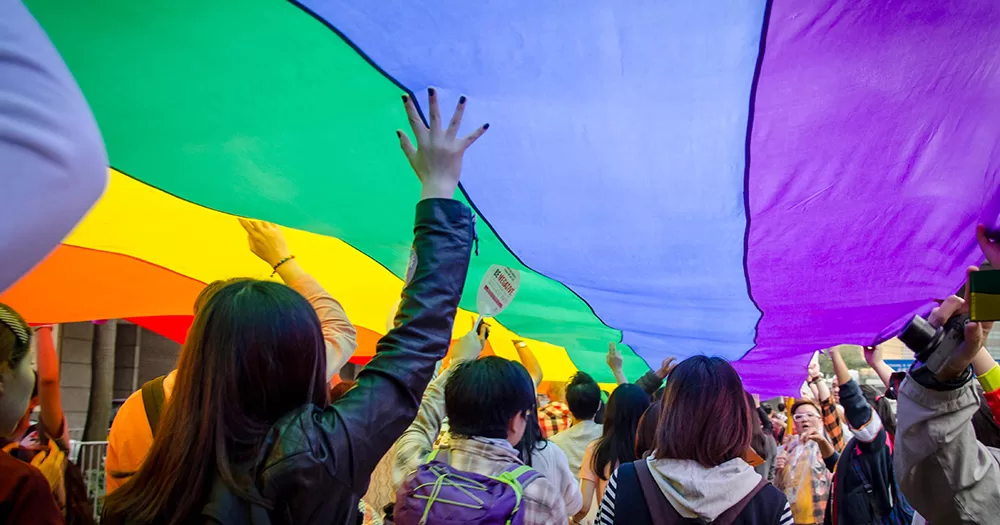 Participant of Hong Kong Pride hold a large rainbow flag above their heads.