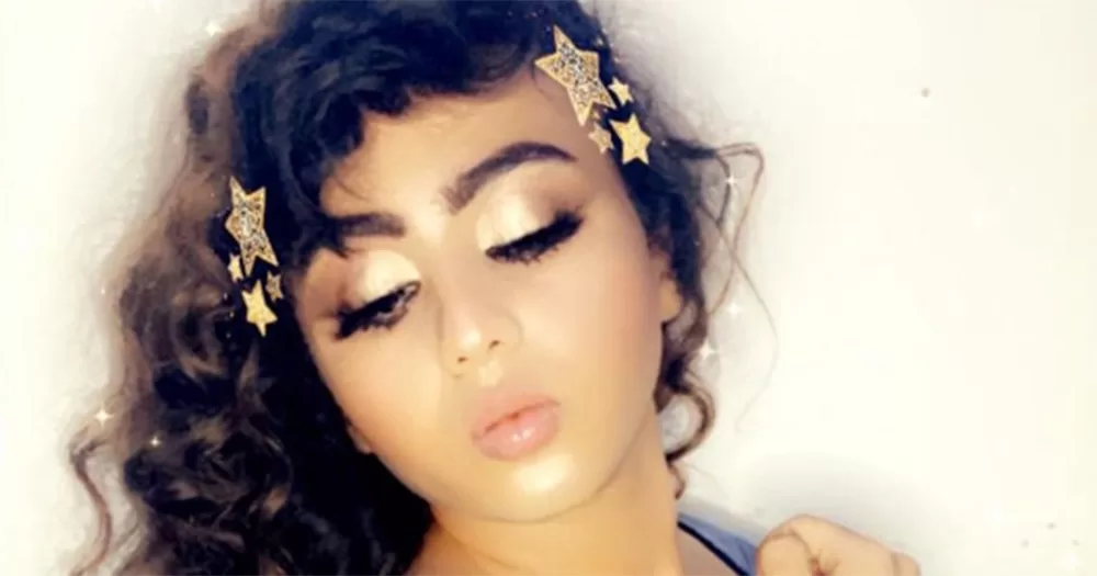 Iraqi TikToker Noor BM. The image is cropped on their face. They have visible eye makeup and thick eyelashes, and have long curly brown hair. They pout their lips and look down.