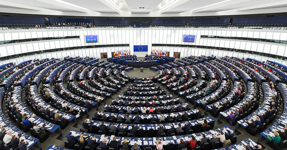Inside the European Parliament in Strasbourg. The image shows a large room with curved rows of seats and curved white walls.