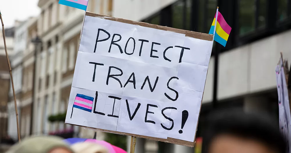 This article is about the Marie Keating Foundation's trans-inclusive aritcle. The image shows a protest sign reading "Protect Trans Lives!" with black text on a white background.