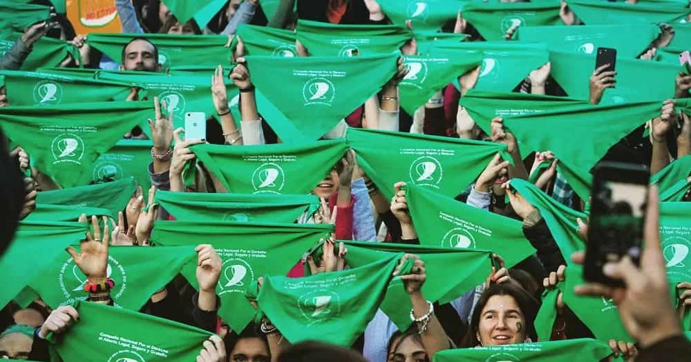 The image shows a crowd holding up green bandanas. The popular movement help the Mexico Supreme Court to rule in favour of removing the ban on abortion.