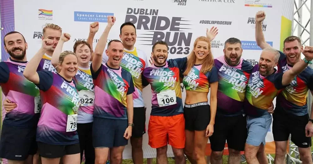 The image shows members of the Dublin Front Runners celebrating after the Pride Run raised over €68,000 for HIV and LGBTQ+ charities. The picture shows 11 people of all genders wearing colourful tshirts which read "Dublin Pride Run 2023". They are cheering and celebrating and raising their fists in the air.