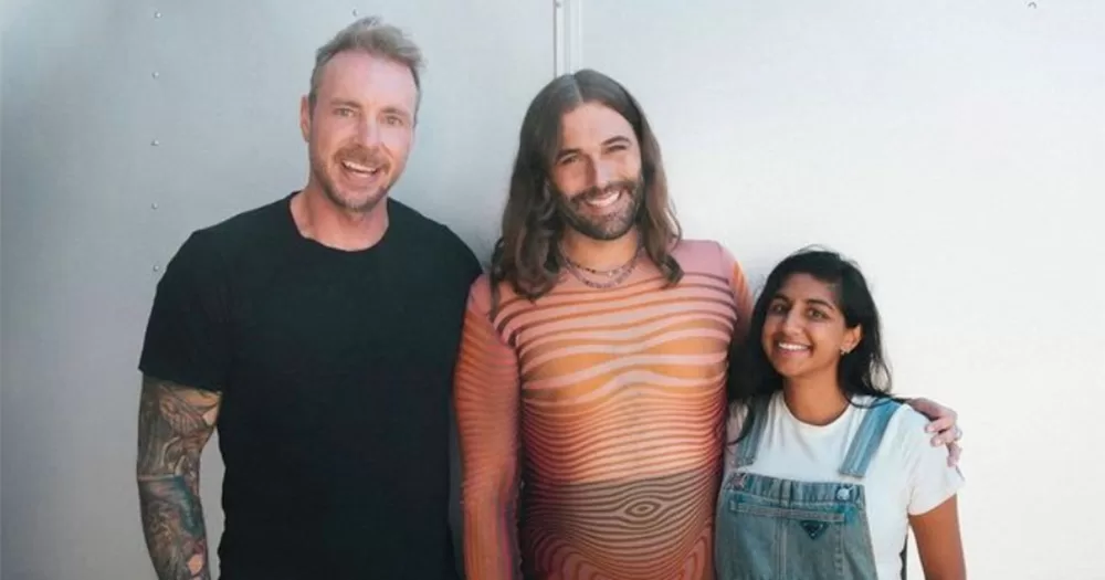 A photo of Dax Shepard, Jonathan Van Ness and Monica Padman. The trio are shown from the waist up, and are posing together smiling.