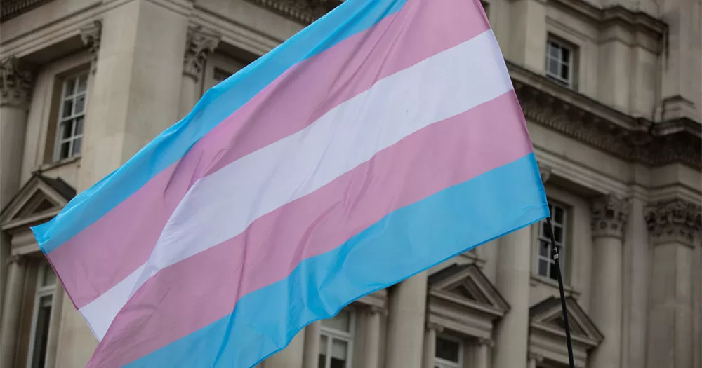 A trans woman has won a case against her employer for being deadnamed. The image shows a trans Pride flag in front of an old building.